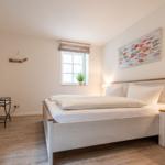 Schlafzimmer mit Bett, Nachttisch, Fernseher und Fenster.