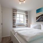 Schlafzimmer mit Doppelbett, Fenster mit Gardinen und Wandbild.