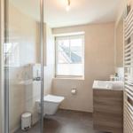 Badezimmer mit Dusche, Toilette, Waschbecken und Fenster