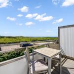 Terrasse mit Tisch und Stühlen, Blick auf grüne Landschaft und Meer.
