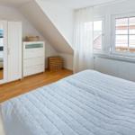 Schlafzimmer mit Dachschrägen, Bett, Kleiderschrank und Fenster.
