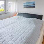Schlafzimmer mit Doppelbett, Fenster und Nachttisch mit Lampe.