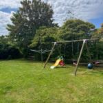 Hinterhof mit Spielplatz, Schaukel und Rutsche auf grünem Rasen.