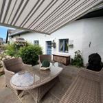 Terrasse mit Sitzgruppe unter Markise, weiße Hauswand und Garten mit Steinmauer.