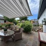 Terrasse mit Markisen, Gartenmöbeln und Steinmauer. Hinterhof mit Pflanzen und Steinweg.