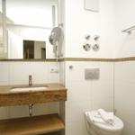 Badezimmer mit Waschbecken, Spiegel und Toilette. Wandverkleidung mit Mosaikstreifen.