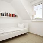 Schlafzimmer mit weißem Bett, Bücherregal und Fenster.