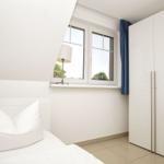 Schlafzimmer mit weißem Bett, Fenster und Kleiderschrank.