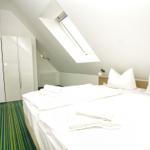 Schlafzimmer mit Dachfenster, Bett und Kleiderschrank. Grün-weißer Teppich. Tür zum Bad.