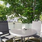 Terrasse mit Tisch und zwei Stühlen, umgeben von Bäumen und Häusern im Hintergrund.