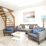 Wohnzimmer mit Sofa, zwei Sesseln und Treppe zur oberen Etage.