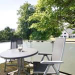 Terrasse mit Tisch und zwei Stühlen. Blick auf grüne Bäume und ein Haus.