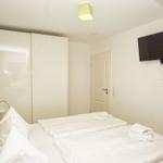 Schlafzimmer mit Bett, Kleiderschrank und Wandfernseher.
