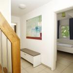 Hausflur mit Holzgeländer, Wandbild und Blick in Schlafzimmer mit Bett und Fenster.