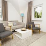 Wohnzimmer mit Sofa, zwei Sesseln, Tisch und Fenstern.