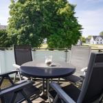 Terrasse mit Tisch und vier Stühlen. Blick auf Grünflächen und Häuser.