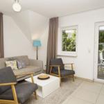 Wohnzimmer mit Sofa, zwei Sesseln und Glastür zur Terrasse.