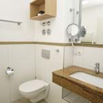 Bathroom with toilet, sink, and mirror. Wooden shelf and chrome fixtures.
