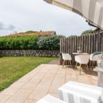 Terrace with seating, awning, and view of green garden with stone wall.