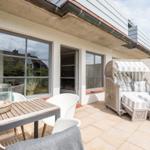 Terrace with lounge furniture, table and chairs. White wall and large windows.