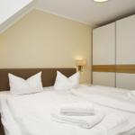 Double bed with white linens and towels, nightstands and wardrobe under sloped ceiling.