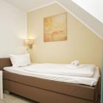 A bedroom with bed, nightstand, and wall lighting. A picture hangs on the wall.
