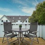 Terrace with table and two chairs. Background: white house and trees.