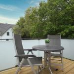 Terrace with table and two chairs, surrounded by trees and a house in the background.