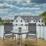 Terrasse mit Tisch und zwei Stühlen, Blick auf weiße Häuser und Bäume unter blauem Himmel.