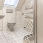 Badezimmer mit Toilette, Waschbecken und Dusche unter Dachschrägen.