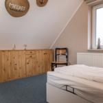 Schlafzimmer mit Bett, Holzschrank und Stuhl unter schrägem Dach