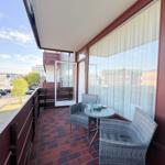 Balkon mit Tisch und zwei Stühlen, roter Fliesenboden und Blick auf die Straße.