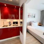 Küche mit roten Schränken und Schlafzimmer mit Bett und Vorhängen.