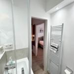 Badezimmer mit Dusche und Heizkörper, Blick in Schlafzimmer mit Bett und Wandbild.