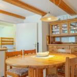Dining area with round table and wooden chairs. Kitchen counter and glass cabinet are visible.