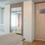 Bedroom with bed, wardrobe, and two white chairs.