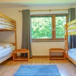 Room with two wooden beds, window with view of trees and wooden floor with rug.