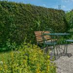 Garden with table, chairs, and hedge. Lawn area and flower bed visible.
