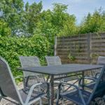 Outdoor area with table and chairs, surrounded by greenery and wooden fence.