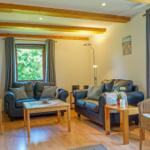 Living room with two sofas, two chairs, and wooden floor. Wooden ceiling beams and windows with curtains.
