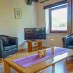 Zwei schwarze Ledersessel stehen um einen Holztisch mit lila Tischläufer. Fernseher und Fenster sind sichtbar.
