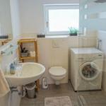 Badezimmer mit Waschmaschine, Toilette und Spiegel