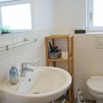 Badezimmer mit Waschbecken, Spiegel, Toilette und Holzregal.