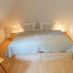 Schlafzimmer mit Dachschrägen, Holzboden, Bett und Nachttischen.