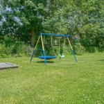 Garten mit Schaukel und Holzterrasse. Umgeben von Bäumen und Gras.