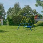 Garten mit Schaukel und Spielplatz. Hinterhof mit Hecke und kleinem Haus.
