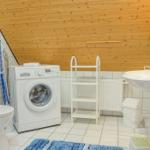 Bathroom with washing machine, sink, and toilet under wooden ceiling.