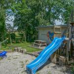Backyard with playground, slide, and swing. Green lawn and wooden play equipment.