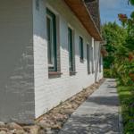 White house wall with green window frames and stone path beside flower beds.