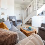 Wohnzimmer mit Sofa, Sessel und Küchenbereich unter einer Treppe.